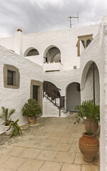 Stone courtyard, whitewashed walls and arched doorways,  cobblestone flooring, potted plants,  small tree and flowers, in the Monastery of Saint John the Theologian on the island of Patmos, Greece.