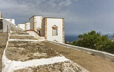 Whitewashed building with reddish-brown stone  featuring a curved rust-colored roof of a chapel  in the foreground in the Monastery of Saint John the Theologian of Patmos, Greece.
