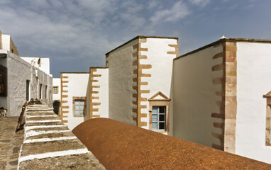 Whitewashed building with reddish-brown stone  featuring a curved rust-colored roof of a chapel  in the foreground in the Monastery of Saint John the Theologian of Patmos, Greece.
