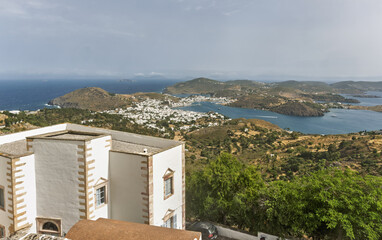 Whitewashed building with reddish-brown stone  featuring a curved rust-colored roof of a chapel  in the foreground in the Monastery of Saint John the Theologian of Patmos, Greece.