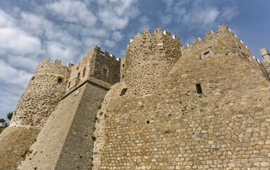 Historic stone fortress with cylindrical tower and crenellated walls surrounding the Monastery of Saint John the Theologian of Patmos, Greece.