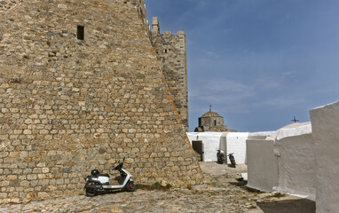 Historic stone fortress with cylindrical tower and crenellated walls surrounding the Monastery of Saint John the Theologian of Patmos, Greece.