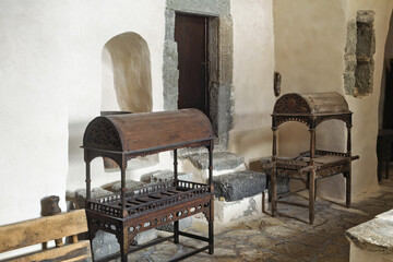 Interior of a historic stone hall with long tables featuring built-in basins, arched doorways, stone walls, wooden benches, in the Monastery of Saint John the Theologian in Patmos, Greece