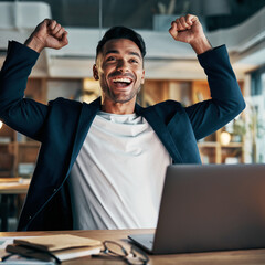 Mężczyzna siedzący za biurkiem przy laptopie podnosi do góry ręce w geście radości z odniesionego sukcesu