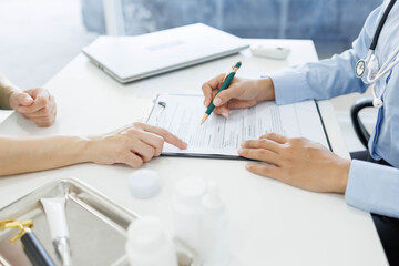 A woman is talking to a man in a medical setting. The woman is holding a pen and the man is holding...