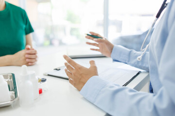 A woman is talking to a man in a medical setting. The woman is holding a pen and the man is holding his hand up. There are several bottles and a laptop on the table. Scene is serious and professional
