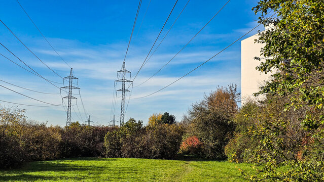 High-voltage power lines over green field and trees, electricity transmission in nature
