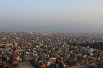 Fototapeta premium A vast aerial view of a densely packed urban landscape stretching toward the horizon under a hazy evening sky.
