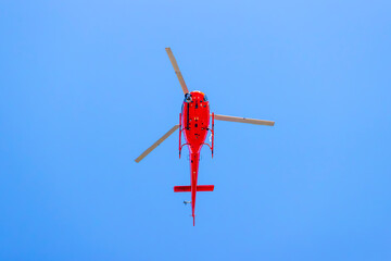 Photograph of a red helicopter in flight filming a sporting event in regional Australia