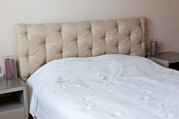 Bedroom interior. Elegant bedroom showcasing beige headboard with tufted design, complemented by cozy white bedspread and soft ambient lighting, creating serene and inviting atmosphere for relaxation