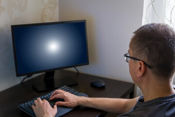 Remote work from home. Man seated at home office desk, focused on typing on computer keyboard, with blank screen in front, creating cozy and productive workspace environment