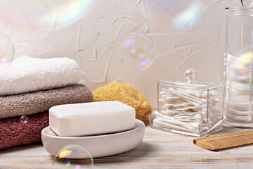 Health and hygiene. White soap bar placed on dish, surrounded by neatly folded towels and bathroom accessories, with colorful bubbles floating in air, creating serene and clean atmosphere