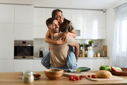 Carefree couple having fun while piggybacking in dining room.