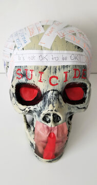 A human skull with glowering red eyes and emblazoned with red letters above the brow spelling the word "Suicide" and a silence finger gesture over the mouth representing suppression (Photo 1). 