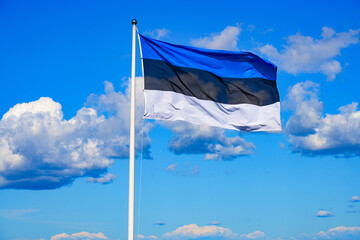 Estonian flag with white, black and blue striped waving in front of a blue sky background