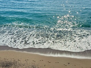 Sparkling sea waves touching sandy beach under sunlight