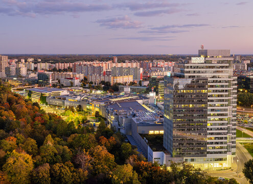 Bratislava, Slovakia - October 18, 2025: Modern cityscape of Bratislava Petrzalka at dusk, a tall glass bank building of Wood et Company, residential blocks and trees with autumn foliage