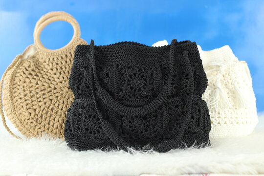 Crocheted bags in different colors and varieties arranged on a white fluffy blanket in front of a blue background.