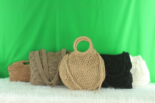 Crocheted bags in different colors and varieties arranged on a white fluffy blanket in front of a green background.