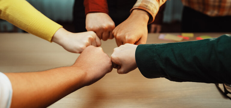A group of diverse individuals showcases teamwork through a fist bump gesture, symbolizing unity and support in a collaborative office environment. SACTR