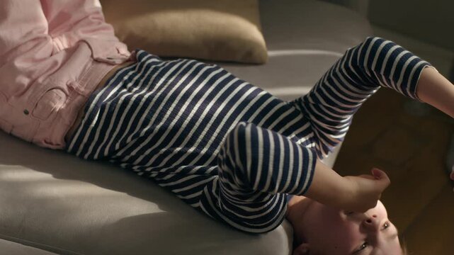 Caucasian girl child kid with mobile phone lying on sofa upside down laughing funny joyful laugh smile watching humorous video using smartphone gadget addict preteen daughter online internet scrolling