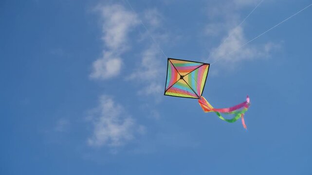 Vibrant diamond kite with colorful streamers dances joyfully against a clear blue sky, embodying freedom and playful spirit