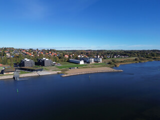 Aerial view of Haderslev Harbor in Denmark with waterfront buildings, green spaces and clear blue sky. Urban meets nature in scenic harmony.