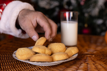 Santa Claus is taking a cookie from a plate next to a glass of milk