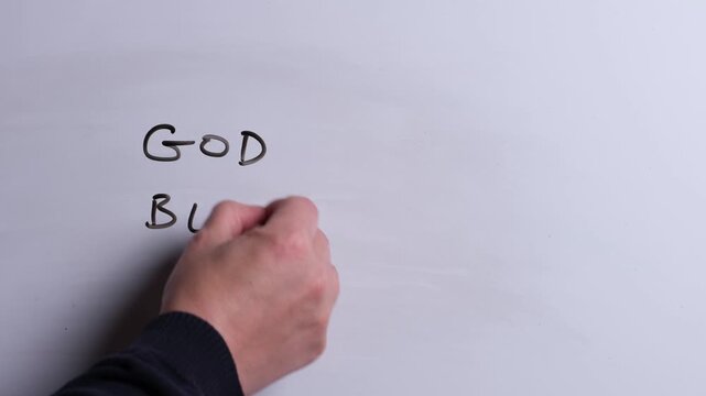 A person is writing God Bless You in black marker pen on a whiteboard, perfect for Christian, religious themes, Church communications or faith presentations