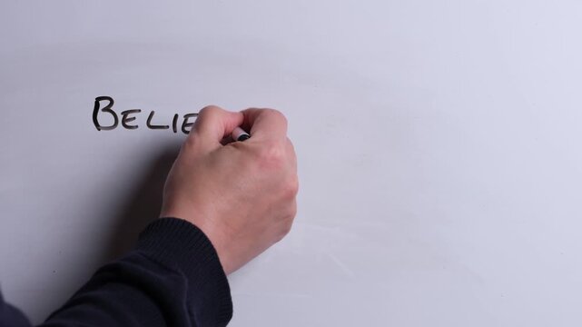 A person is writing Believe in Miracles in black marker pen on a whiteboard, perfect for Christian, religious themes, Church communications or faith presentations