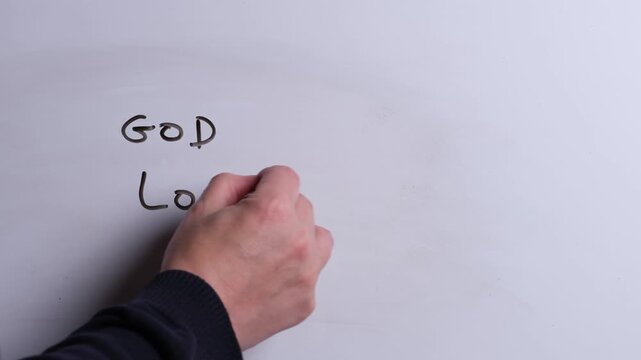 A person is writing God Loves You in black marker pen on a whiteboard, perfect for Christian, religious themes, Church communications or faith presentations