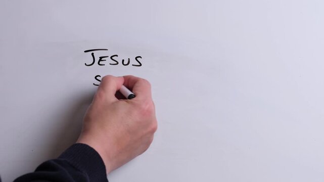 A person is writing Jesus Saves All in black marker pen on a whiteboard, perfect for Christian, religious themes, Church communications or faith presentations