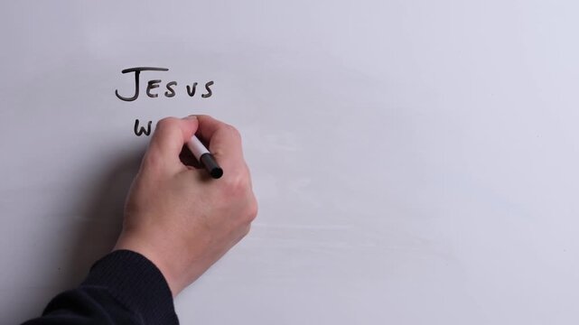 A person is writing Jesus Welcomes All in black marker pen on a whiteboard, perfect for Christian, religious themes, Church communications or faith presentations