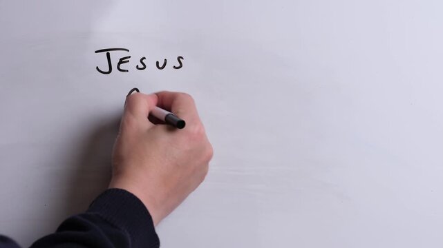 A person is writing Jesus Above All in black marker pen on a whiteboard, perfect for Christian, religious themes, Church communications or faith presentations