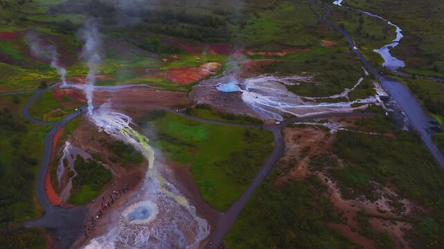 High, slow aerial view shows turquoise boiling pools, white silica fans, fumaroles, walkways, road and river near Myvatn, North Iceland, with visitors and soft daylight