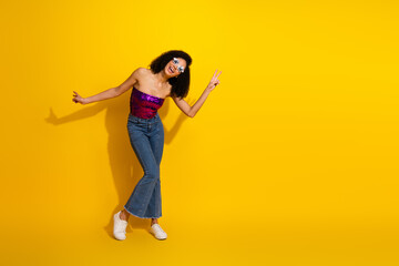 Young stylish woman dancing in a bright yellow background wearing casual chic top and jeans