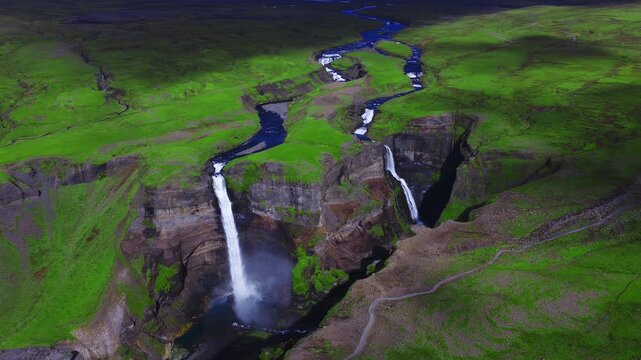 Aerial view shows Haifoss and Granni plunging into a basalt canyon in Thjorsardalur, Iceland, with braided river, summer greens, mist, and layered volcanic rock. Stranger Things waterfall.