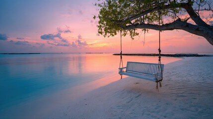 A rustic rope swing hanging from a tree branch on a sandy beach during a vibrant orange and pink sunset over calm water.