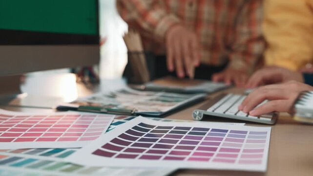 Team members collaborate in a modern office, surrounded by color swatches and design tools, showcasing creativity and teamwork in graphic design projects. SACTR