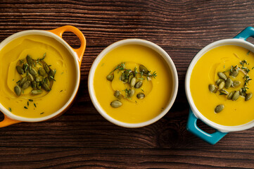 Pumpkin soup in ceramic bowls, wooden background, top view