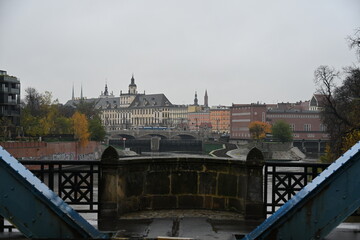 Steel suspension bridge with a view of Wrocław Old Town on a cloudy day
