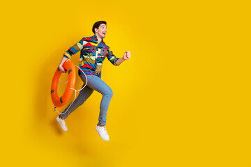 Young man in colorful shirt jumps with life ring against a bright yellow background for bold summer lifestyle and promotional image