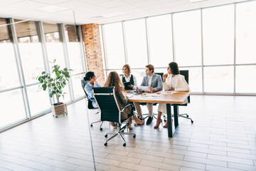Business team collaborating around a table in a modern office workspace with natural lighting, discussing project ideas and strategies