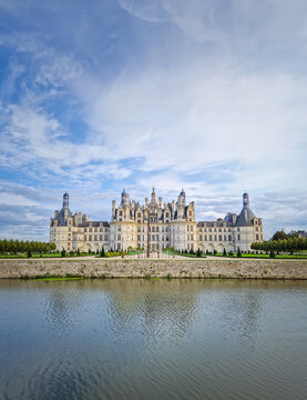The symmetrical Ch&acirc;teau de Chambord is reflected in the still water, highlighting its magnificent Renaissance architecture with numerous turrets. The majestic castle stands beneath a beautiful sky