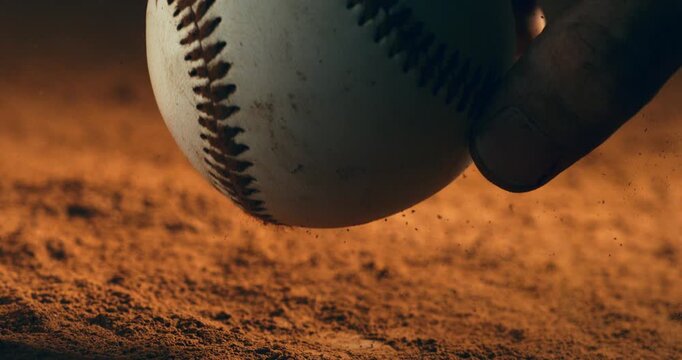 Slow motion close-up of a baseball is taken by athlete hand on dusty ground under dramatic light at 1000 fps. Capturing the raw tension and texture of the game.