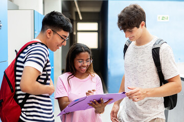 Smiling young diverse students talking and studying together in a high school hallway. Friendship, teamwork and education concept.