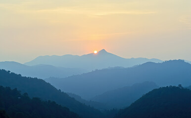 Obraz premium Golden sun crests hazy blue mountain range at dawn mountains sunrise