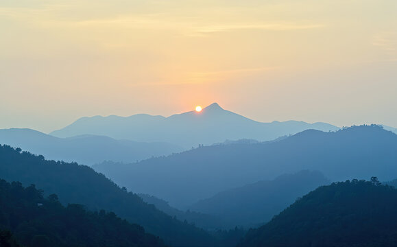Golden sun crests hazy blue mountain range at dawn mountains sunrise