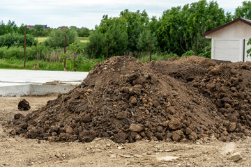 Soil pile near construction site with green trees and building in background on a cloudy day