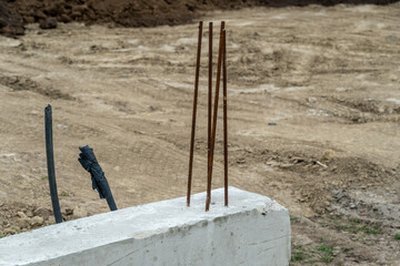 Construction site with rebar sticking out of a concrete block surrounded by dirt in an unfinished area during daylight hours